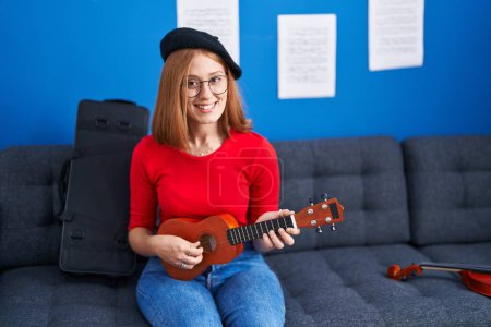Téléchargez les photos : Jeune rousse femme musicien souriant confiant jouer ukulele au studio de musique - en image libre de droit