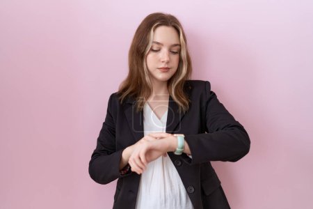 Téléchargez les photos : Jeune femme d'affaires caucasienne portant une veste noire vérifiant l'heure sur la montre-bracelet, détendue et confiante - en image libre de droit