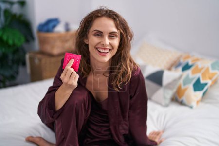 Photo for Beautiful brunette woman holding condom at the bedroom looking positive and happy standing and smiling with a confident smile showing teeth - Royalty Free Image