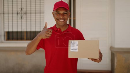 Photo for Young latin man delivery worker holding package doig ok gesture with finger at street - Royalty Free Image