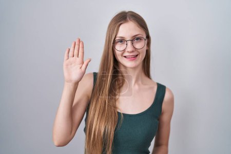 Téléchargez les photos : Jeune femme caucasienne debout sur fond blanc renonçant à dire bonjour heureux et souriant, geste de bienvenue amical - en image libre de droit