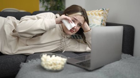 Téléchargez les photos : Young blonde woman watching movie crying on sofa at home - en image libre de droit