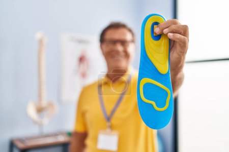 Photo for Middle age man podiatrist holding insole at physiotherpy clinic - Royalty Free Image
