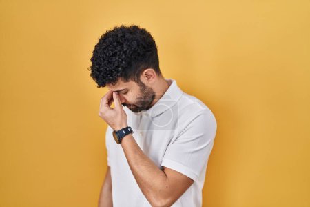 Photo for Arab man standing over yellow background tired rubbing nose and eyes feeling fatigue and headache. stress and frustration concept. - Royalty Free Image