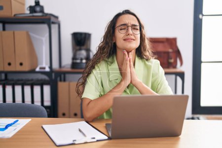 Photo for Young hispanic woman working at the office wearing glasses begging and praying with hands together with hope expression on face very emotional and worried. begging. - Royalty Free Image