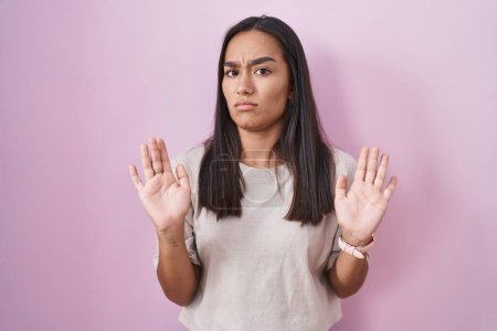 Photo for Young hispanic woman standing over pink background moving away hands palms showing refusal and denial with afraid and disgusting expression. stop and forbidden. - Royalty Free Image