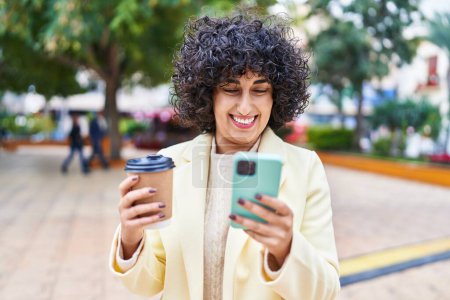 Téléchargez les photos : Jeune femme du Moyen-Orient excutive en utilisant smartphone boire du café au parc - en image libre de droit