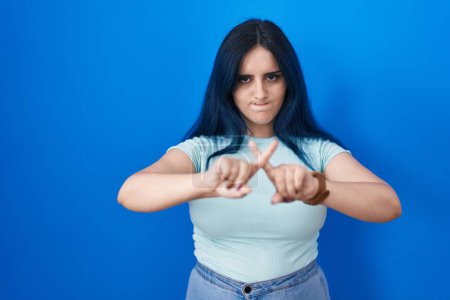 Téléchargez les photos : Jeune fille moderne avec les cheveux bleus debout sur fond bleu expression de rejet en croisant les doigts faisant signe négatif - en image libre de droit