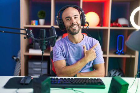 Photo for Middle age bald man playing video games wearing headphones smiling cheerful pointing with hand and finger up to the side - Royalty Free Image