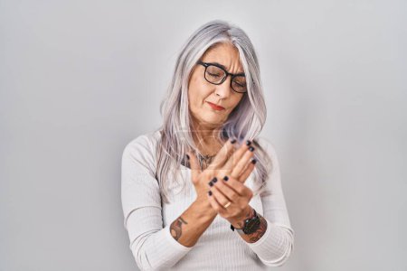 Téléchargez les photos : Femme d'âge moyen avec les cheveux gris debout sur fond blanc souffrant de douleur aux mains et aux doigts, inflammation de l'arthrite - en image libre de droit