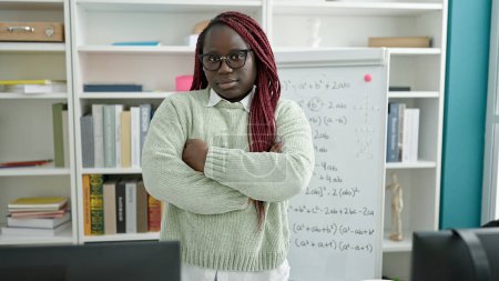 Photo for African woman with braided hair standing by white with crossed arms at university library - Royalty Free Image