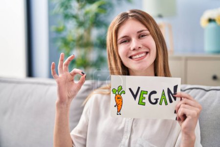 Photo for Beautiful woman holding banner with vegan word doing ok sign with fingers, smiling friendly gesturing excellent symbol - Royalty Free Image