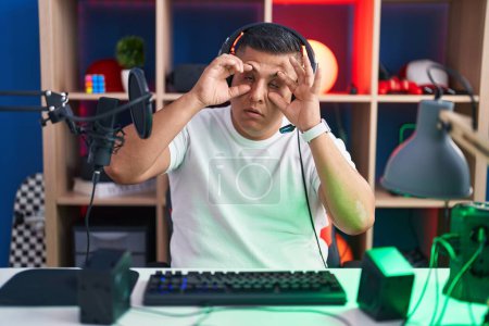 Photo for Young hispanic man playing video games trying to open eyes with fingers, sleepy and tired for morning fatigue - Royalty Free Image