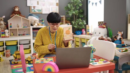 Foto de Joven mujer china maestra de preescolar que tiene lección de vocabulario en línea en el jardín de infantes - Imagen libre de derechos