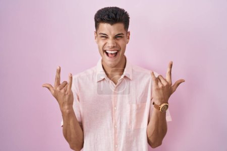 Photo for Young hispanic man standing over pink background shouting with crazy expression doing rock symbol with hands up. music star. heavy music concept. - Royalty Free Image