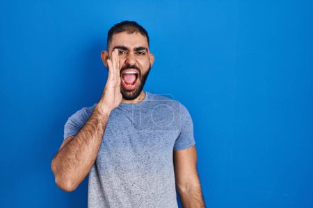 Photo for Middle east man with beard standing over blue background shouting and screaming loud to side with hand on mouth. communication concept. - Royalty Free Image