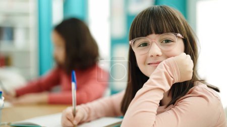 Photo for Adorable hispanic girl student writing on notebook at classroom - Royalty Free Image