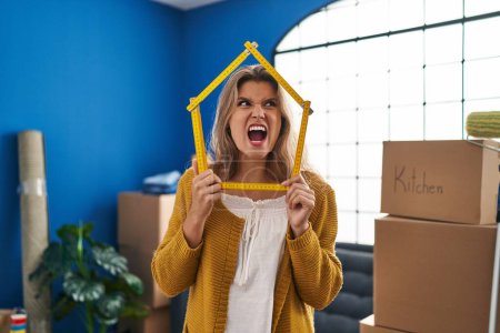 Photo for Young woman standing at new home angry and mad screaming frustrated and furious, shouting with anger. rage and aggressive concept. - Royalty Free Image
