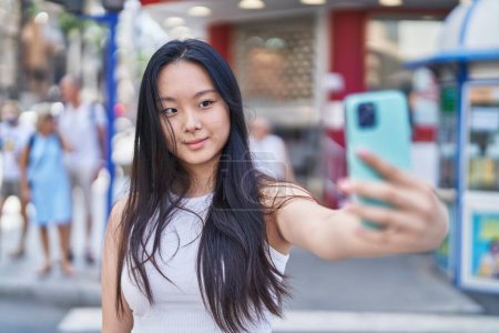 Foto de Young chinese woman smiling confident making selfie by the smartphone at street - Imagen libre de derechos