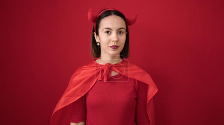 Téléchargez les photos : Jeune belle femme hispanique portant costume diable avec expression détendue sur fond rouge isolé - en image libre de droit