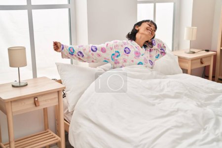 Foto de Joven hermosa mujer hispana despertando estirando los brazos en el dormitorio - Imagen libre de derechos