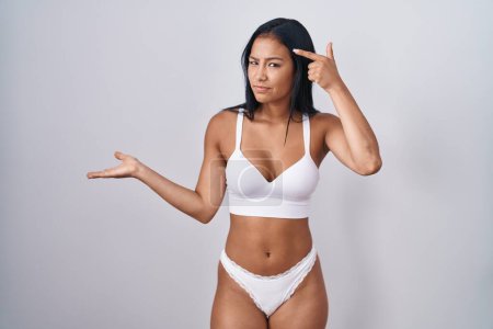 Téléchargez les photos : Femme hispanique portant lingerie confus et agacé avec la paume ouverte montrant l'espace de copie et pointant du doigt vers le front. Penses-y.. - en image libre de droit
