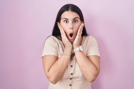 Photo for Young hispanic woman standing over pink background afraid and shocked, surprise and amazed expression with hands on face - Royalty Free Image