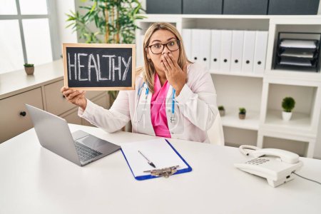 Photo for Young hispanic doctor woman holding healthy word covering mouth with hand, shocked and afraid for mistake. surprised expression - Royalty Free Image