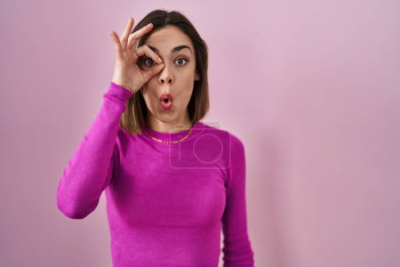 Foto de Mujer hispana de pie sobre fondo rosa haciendo un gesto bien sorprendido con la cara sorprendida, los ojos mirando a través de los dedos. expresión incrédula. - Imagen libre de derechos