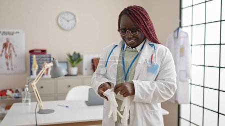 Téléchargez les photos : Femme africaine avec médecin cheveux tressés mettre des gants pour la sécurité à la clinique - en image libre de droit