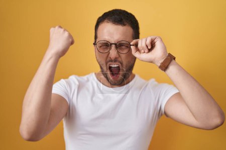 Téléchargez les photos : Homme hispanique tenant des lunettes agacé et frustré criant de colère, hurlant fou de colère et la main levée - en image libre de droit