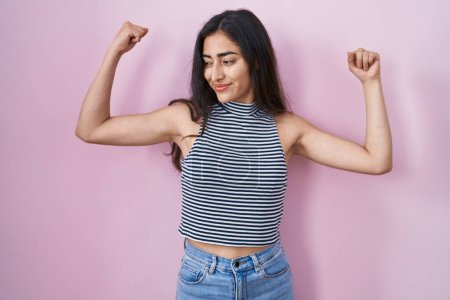 Photo for Young teenager girl wearing casual striped t shirt showing arms muscles smiling proud. fitness concept. - Royalty Free Image