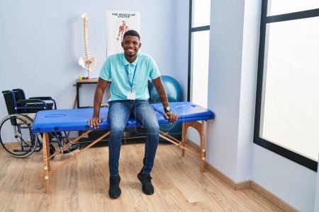 Photo for Young african american man physiotherapist sitting on massage board al rehab clinic - Royalty Free Image
