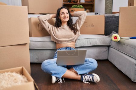 Foto de Mujer hispana joven usando portátil sentado en el piso en casa nueva - Imagen libre de derechos
