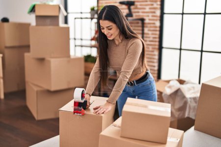 Photo for Young beautiful hispanic woman smiling confident packing cardboard box at new home - Royalty Free Image