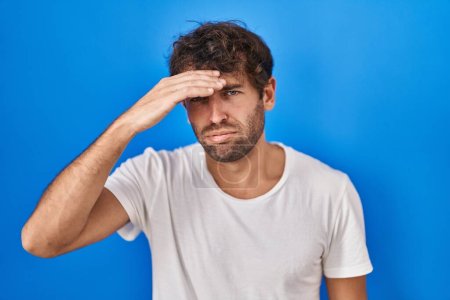 Photo for Hispanic young man standing over blue background worried and stressed about a problem with hand on forehead, nervous and anxious for crisis - Royalty Free Image