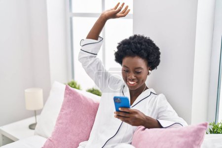 Téléchargez les photos : Young african american woman listening to music sitting on bed at bedroom - en image libre de droit