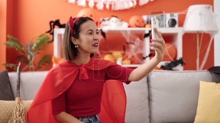 Téléchargez les photos : Jeune belle femme hispanique portant costume diable faire selfie par smartphone à la maison - en image libre de droit