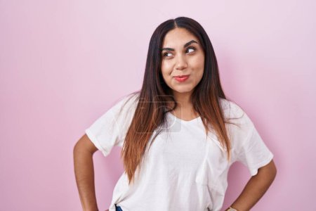 Téléchargez les photos : Jeune femme arabe debout sur fond rose souriant regardant vers le côté et regardant loin en pensant. - en image libre de droit