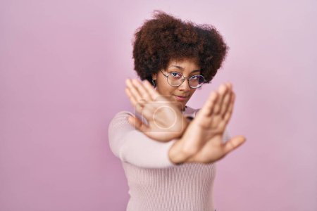 Téléchargez les photos : Jeune femme afro-américaine debout sur fond rose expression de rejet croisant les bras et les paumes faisant signe négatif, visage en colère - en image libre de droit