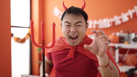 Foto de Joven hombre chino con traje de diablo haciendo gesto de miedo en casa - Imagen libre de derechos