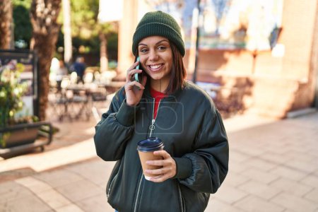 Téléchargez les photos : Jeune belle femme hispanique parlant sur smartphone boire du café à la terrasse du café - en image libre de droit