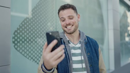 Téléchargez les photos : Jeune homme caucasien souriant sur un appel vidéo à la rue - en image libre de droit