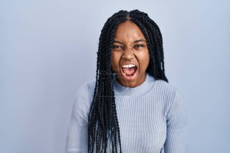 Téléchargez les photos : African american woman standing over blue background angry and mad screaming frustrated and furious, shouting with anger. rage and aggressive concept. - en image libre de droit