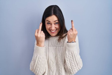 Téléchargez les photos : Young brunette woman standing over blue background showing middle finger doing fuck you bad expression, provocation and rude attitude. screaming excited - en image libre de droit
