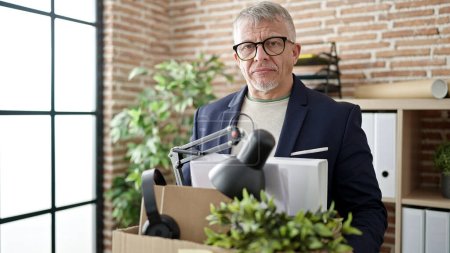 Middle age grey-haired man business worker dismissed holding cardboard box at office