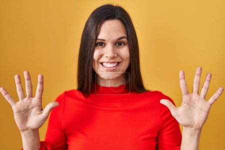 Photo for Young hispanic woman standing over yellow background showing and pointing up with fingers number ten while smiling confident and happy. - Royalty Free Image