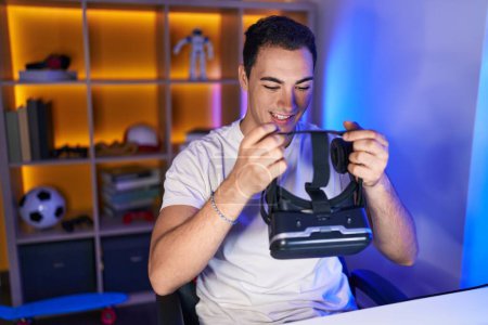 Photo for Young hispanic man streamer smiling confident holding virtual reality glasses at gaming room - Royalty Free Image