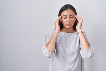 Foto de Mujer hispana joven de pie sobre fondo blanco con la mano en la cabeza, dolor de cabeza porque el estrés. padecer migraña. - Imagen libre de derechos