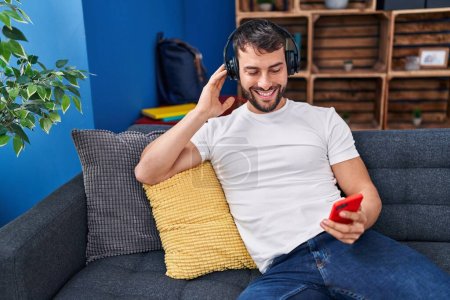 Photo for Young hispanic man listening to music sitting on sofa at home - Royalty Free Image